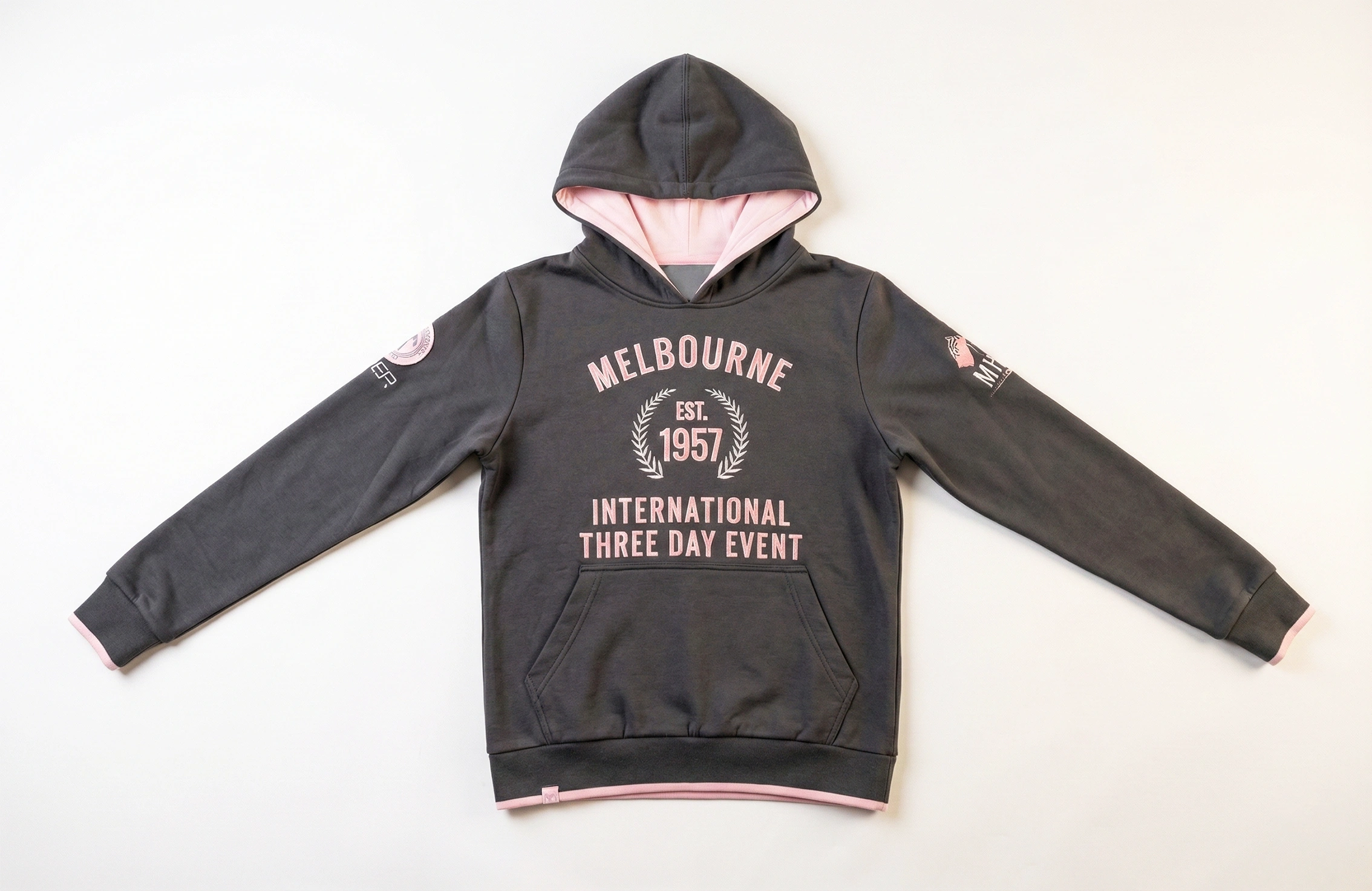 黑色連帽衛衣正面平鋪照，粉紅內帽與飾邊，胸前「MELBOURNE EST. 1957」活動字樣